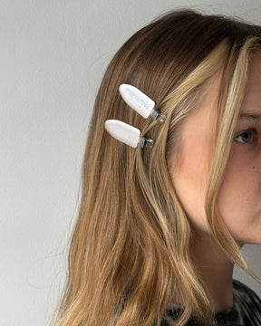 Person wearing a white hair clip with 'Maria Nila' branding on a plain background